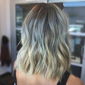 Modelo con cabello rubio, raíces oscuras y balayage gris.