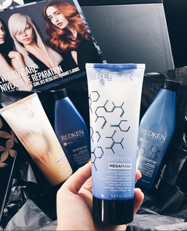 Mano sujetando un envase azul de la mascarilla Extreme Mega Mask de Redken.